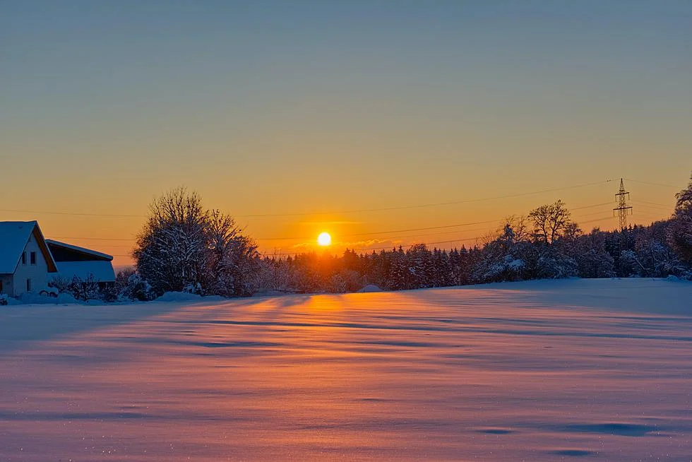 Winter sunrise over snow-covered field with trees and barn