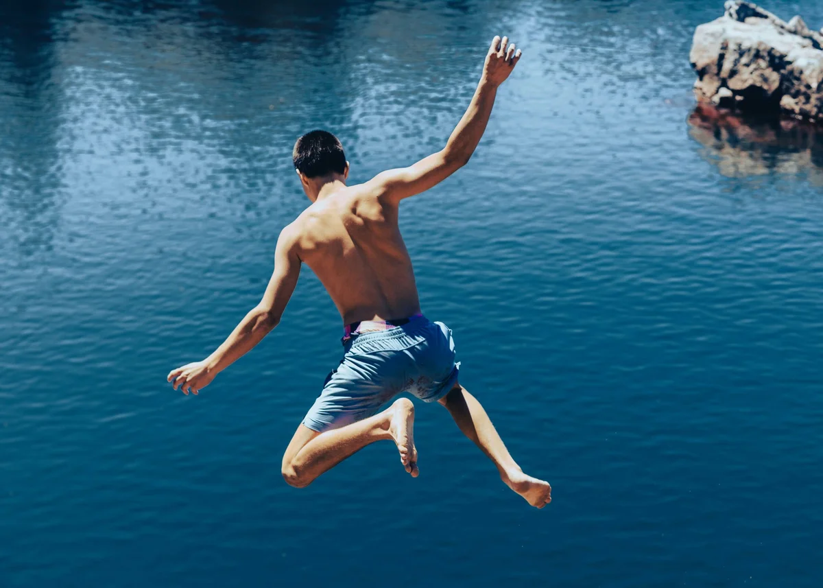 Person mid-jump above clear blue water, letting go of the day