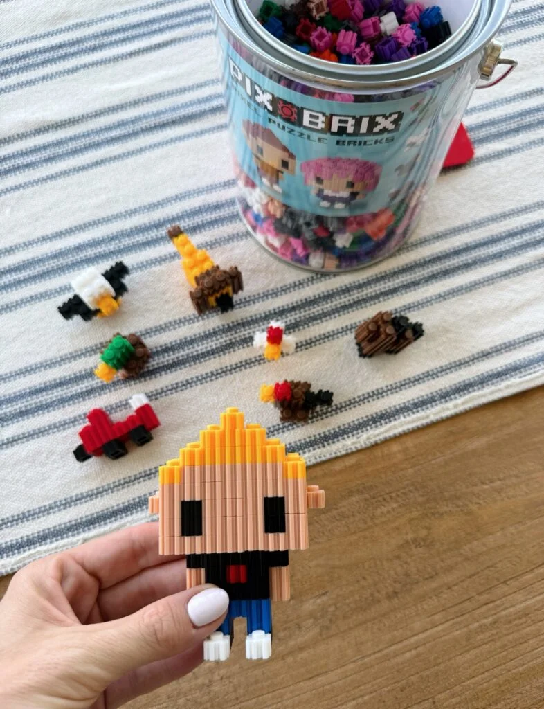 Hands building a pixel-art figure from tiny colorful puzzle bricks