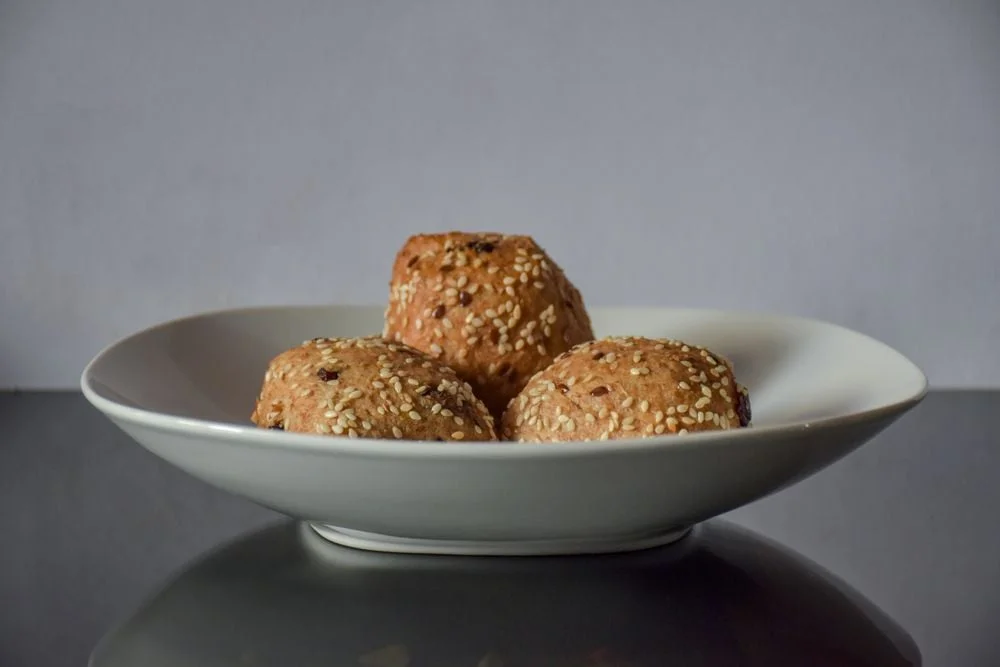 Sesame-topped baked rolls arranged in a white ceramic bowl