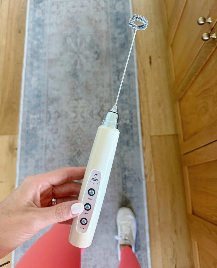 Hand holding a cream rechargeable three-speed handheld drink frother