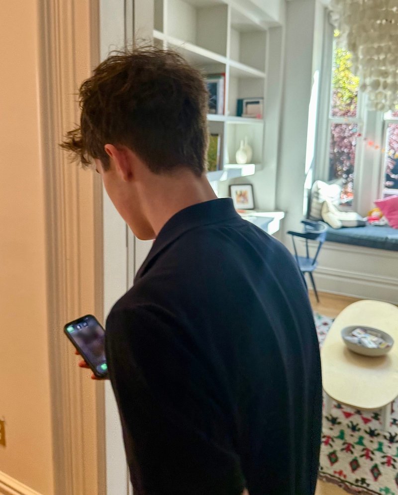 A man in a dark shirt holding his smartphone in a bright living room