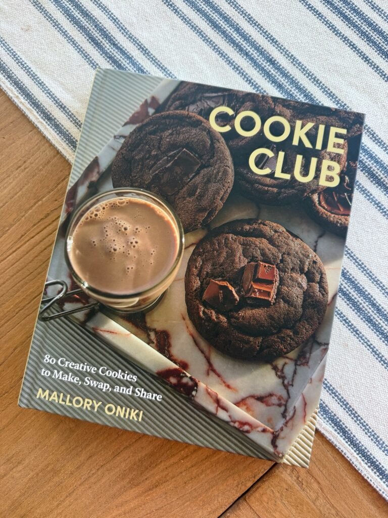 Cookie Club cookbook cover beside frothy hot chocolate on striped cloth
