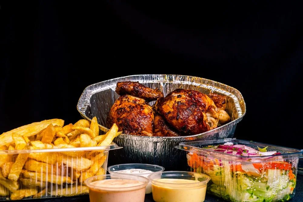 Rotisserie chicken with fries, salad, and dipping sauces in containers
