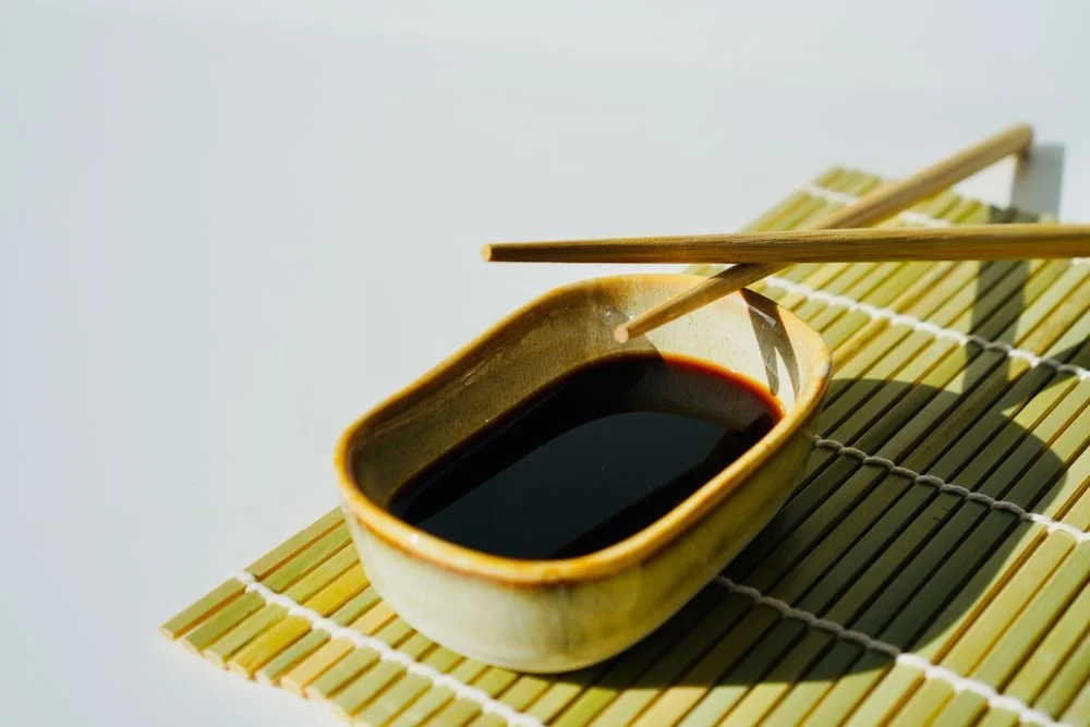 Ceramic dish of soy sauce with chopsticks on a bamboo mat