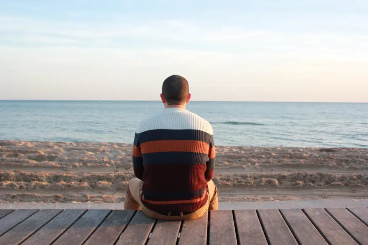 man sitting alone on wooden deck facing calm ocean horizon