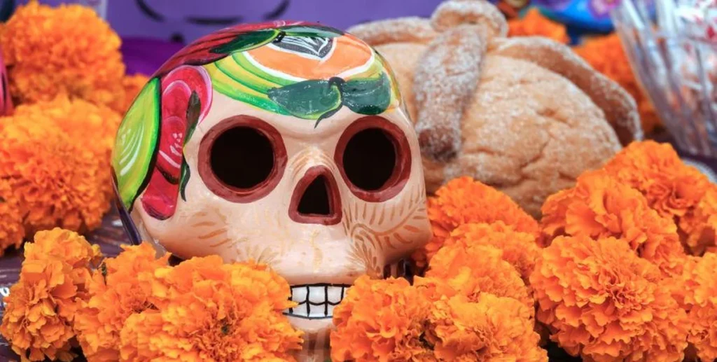 Colorful painted sugar skull surrounded by orange marigold flowers