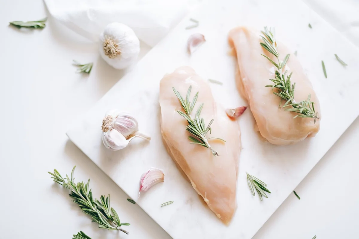 Raw chicken breasts with rosemary and garlic on white marble