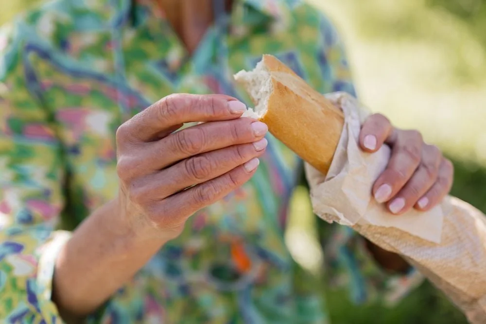 Hands holding a partially eaten baguette wrapped in paper