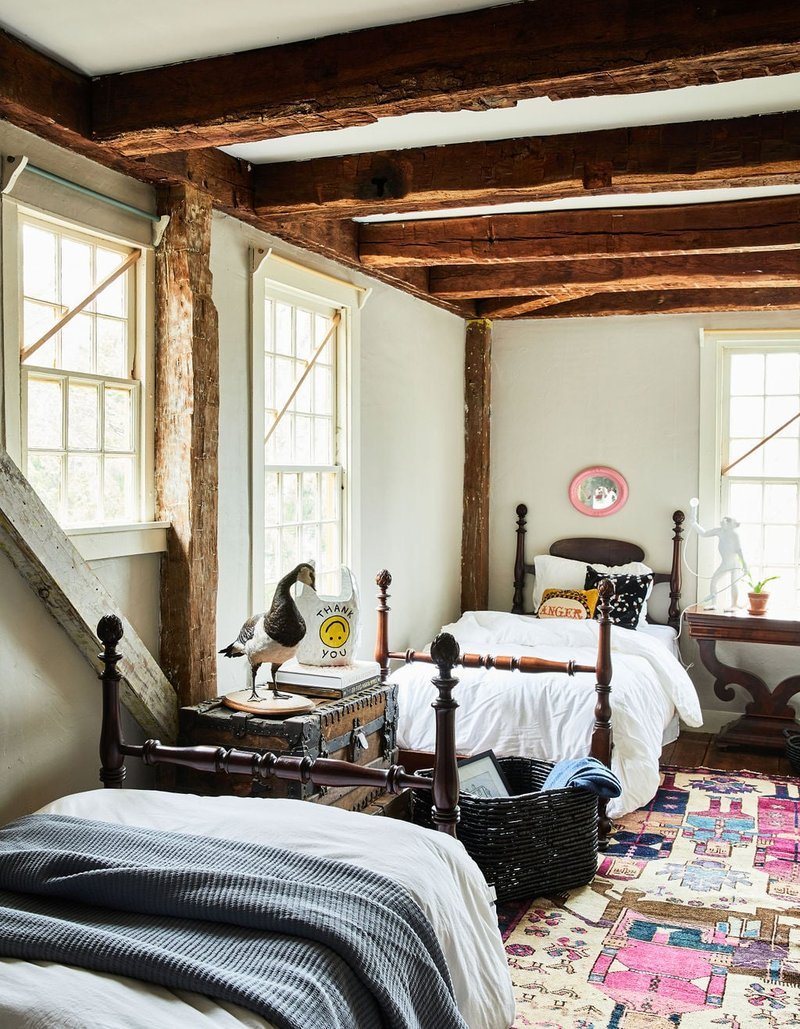 Rustic guest bedroom with exposed wooden beams, two beds, and patchwork rug