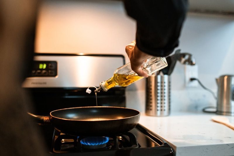 Hand pouring olive oil into a frying pan on a stove